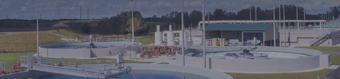 A panoramic view of a water treatment plant with multiple circular and rectangular tanks, pipes, and other equipment. 